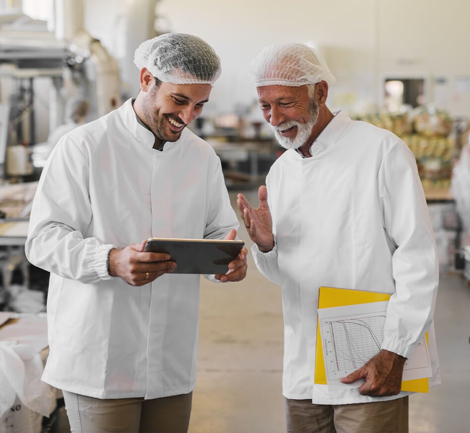 Workers wearing hairnets looking at a tablet.
